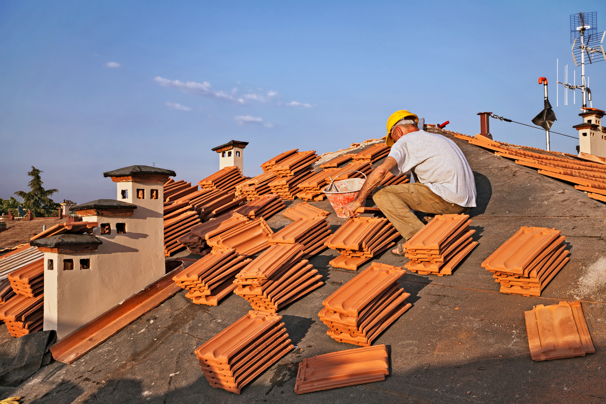 construction worker on a roof covering it with tiles - roof renovation: installation of tar paper, roofing with new tiles and chimney